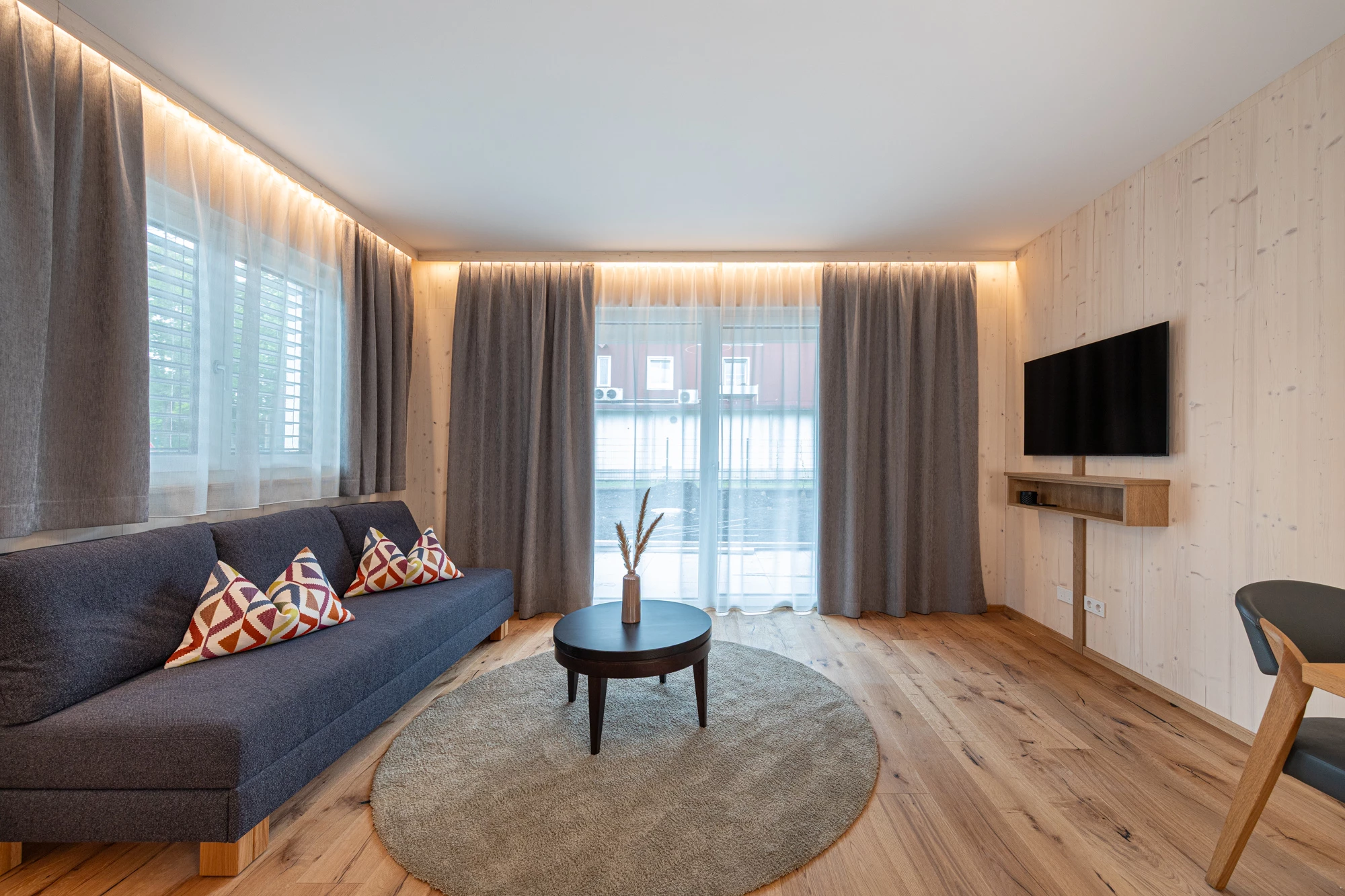Wohnbereich mit Sofa, Wand-TV und Terrassentür