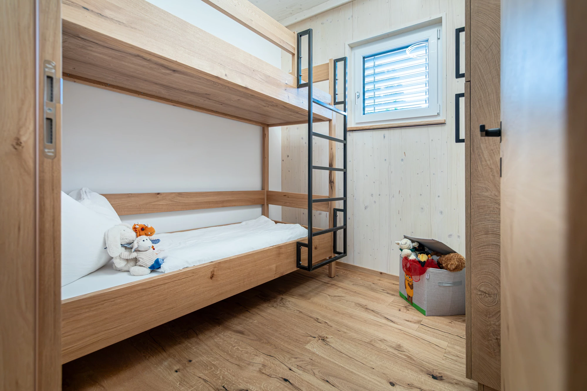 Kinderzimmer mit Etagenbett aus Eichenholz, hellen Holzwänden und Fenster