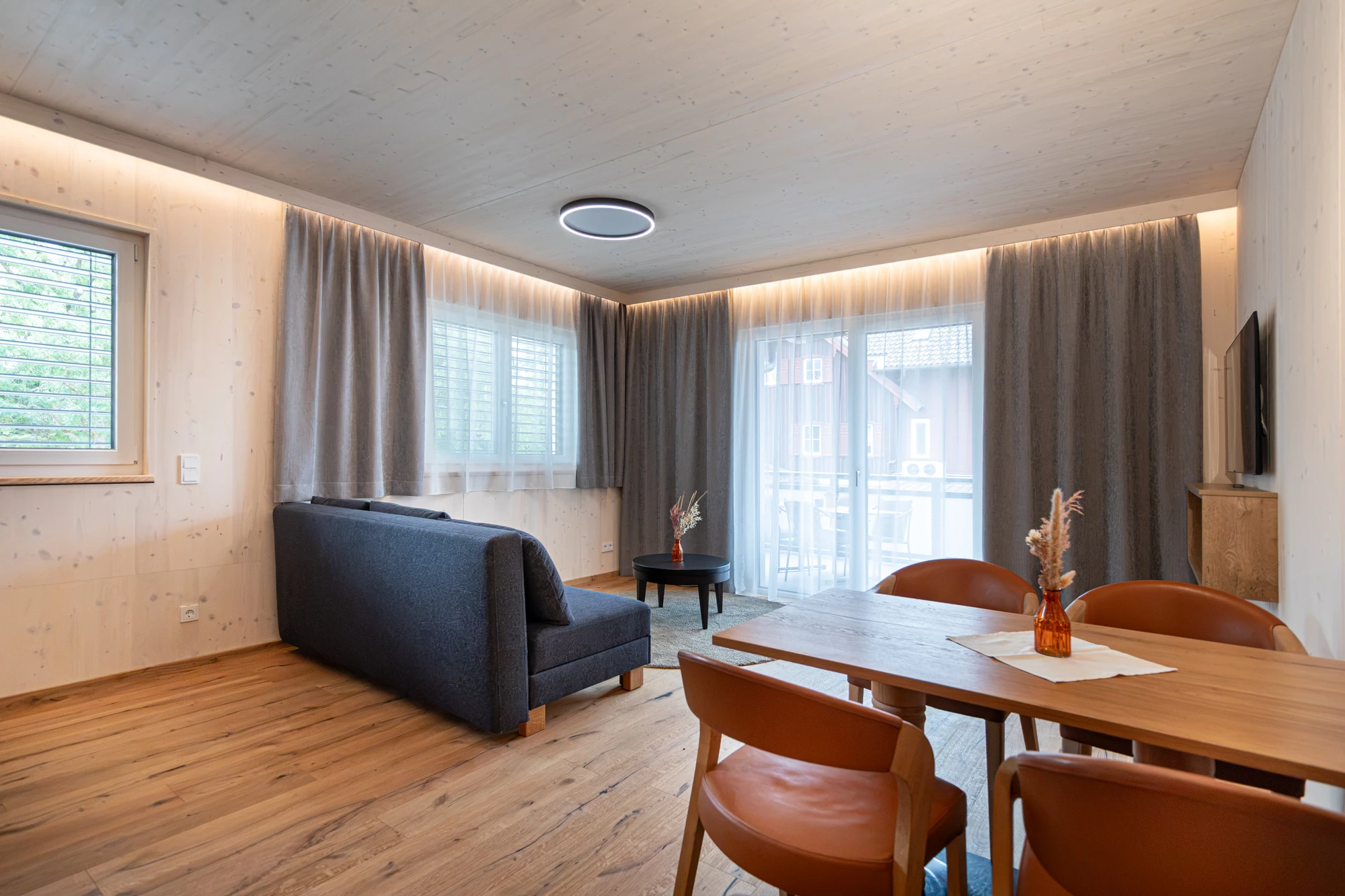 Wohnzimmer mit Sofa, Esstisch und Balkontür